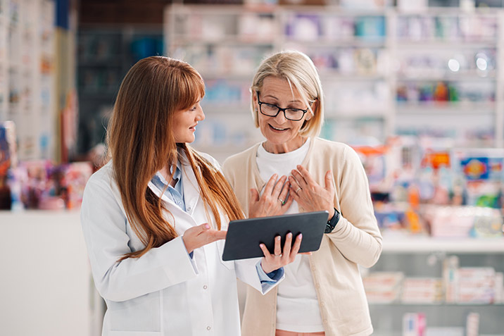 Eine Apothekerin berät mithilfe eines Tablets eine Kundin in der Offizin.